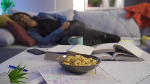 Adult Lying on Couch Behind Books and Snacks