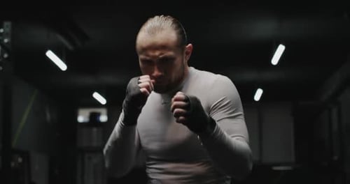 Strong Adult Man Doing Shadow Boxing and Performing Various Punches During Workout in Dark Gym