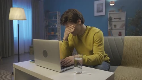 A Man Suffers From an Attack of Headache While Working on a Laptop The Man Squints Rubs His Temples