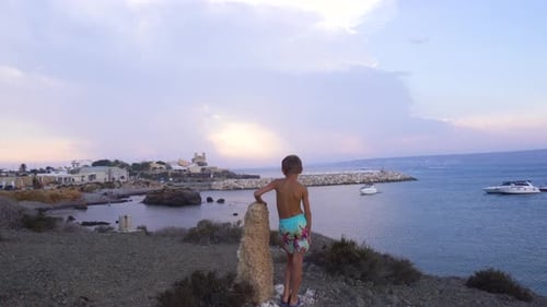 Boy is leaning on the rock and watching over the shore of Spanish island.