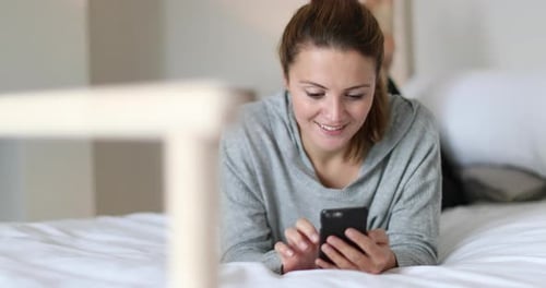 Woman Relaxes on Bed While Using Mobile Phone