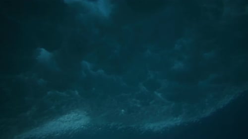 Underwater angle of ocean wave crashing and spreading textured speckled pattern across surface