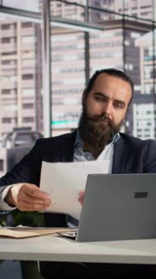 Vertical Video Business Owner Reviews KPIs and Infographics on Documents at Desk
