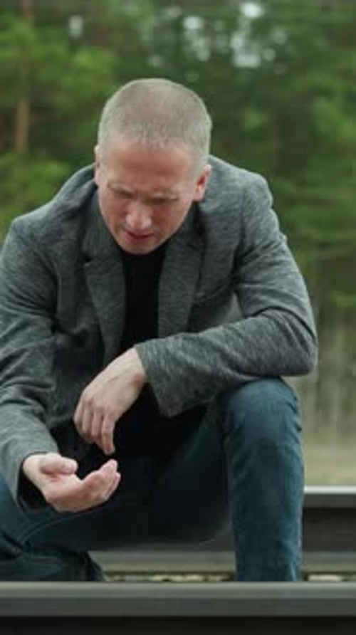 Man Kneeling By Railway Track Examining Closely in a Forest Setting