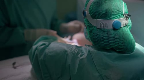 Rückansicht Krankenschwester hilft dem Chirurgen bei der Brusttransplantation in die Brust einer nicht erkennbaren Patientin in
