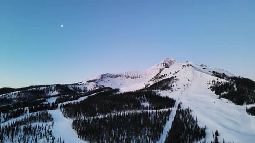 A drone shot of snowy Big Sky, Montana in winter, showcasing the ski resort and majestic mountain te