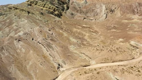 Drone view flying over a curving and winding road at the foot of dry mountains and geologic formatio