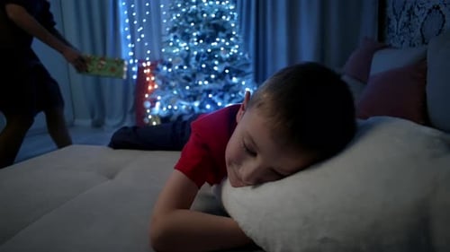 Boy Sleeps as Mother Puts Gift Under Christmas Tree