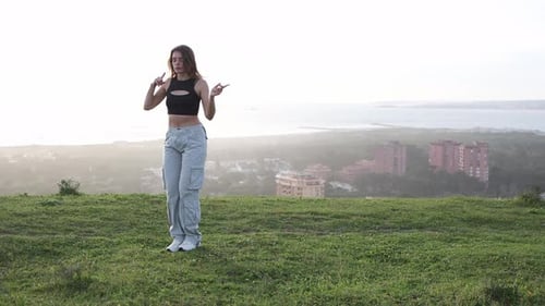 Woman dances on hill overlooking city and ocean