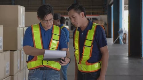 Young man wearing vest standing and talking with colleagues about shipping in the warehouse.