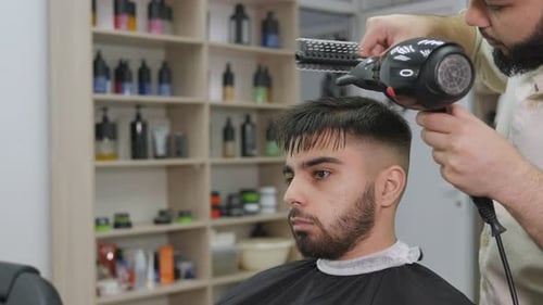 Barber Styles Young Man's Hair With Blower and Comb