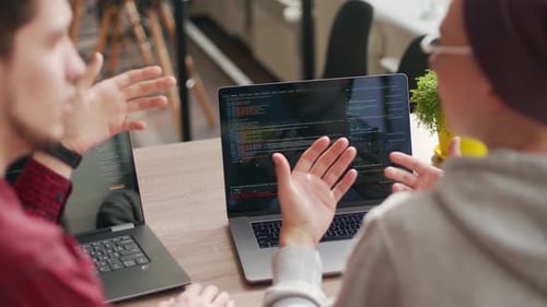 Two Hipster Coworkers Sharing Ideas About Project Sitting with Laptops in Spacious Open Space Office