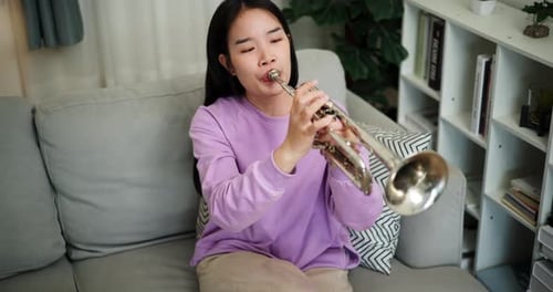 Woman plays trumpet while sitting on couch