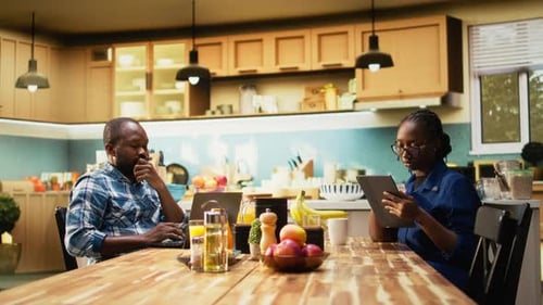 Man and Woman Using Devices at Kitchen Table