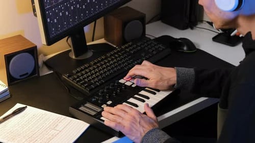 Man Creates Music with Midi Keyboard at Desk