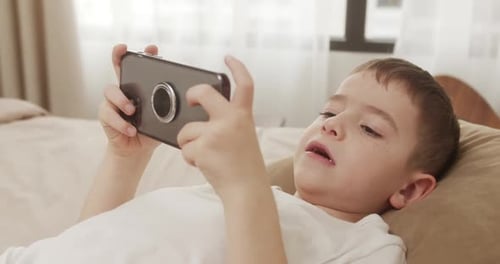 Child Playing on Smartphone While Lying on Bed