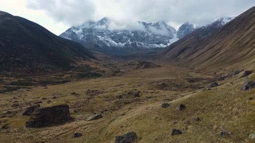 Amazing drone fly at beautiful vast mountain valley with distant snow peaks on wild grassy