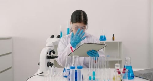 Teenage Girl Scientist Using Microscope and Writing Notes