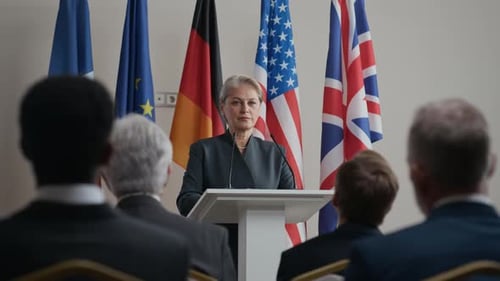 Woman Speaking at Podium with Flags Behind Her