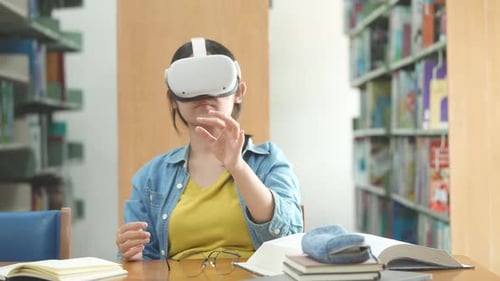 Young Asian female high school student using virtual reality headset in the library.