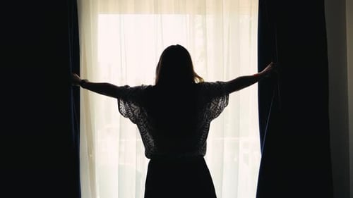 Woman Opens Curtains to Bright Sunlight in Room