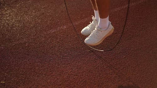 Slow Motion Closeup Legs of an Unrecognizable Athlete in White Sneakers Jumping Rope on a Running