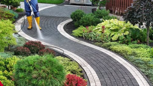 Gardener Using a Pressure Washer to Clean a Beautifully Landscaped Garden Pathway in Spring