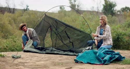 Young Couple Putting Up Tent Outdoors Together