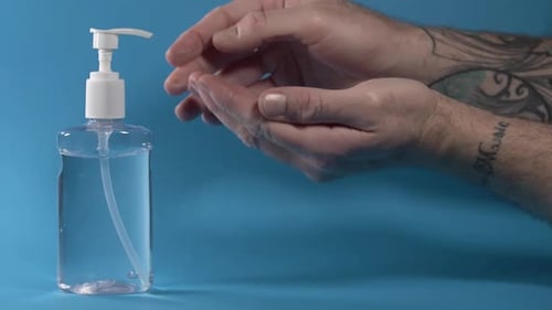 Slow Motion Of Spraying And Rubbing Liquid Sanitizer On Hands In Blue Background - close up
