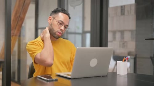 Young Adult Massaging Neck at Desk at Workplace