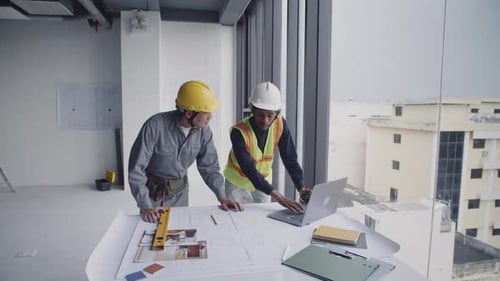 Construction Workers Planning With Blueprints and Laptop