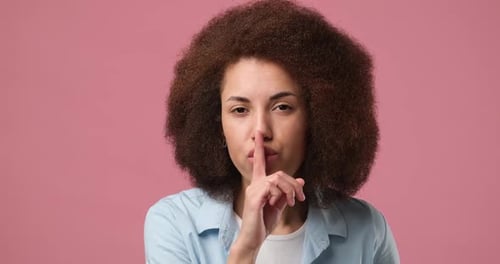 Jovem mulher afro-americana gesticulando o dedo nos lábios sorrindo mostrando um sinal secreto de Keep Silence Hush
