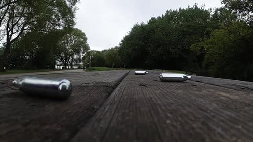 Vários cilindros metálicos de gás de óxido nitroso, droga recreativa em câmera lenta, caindo sobre uma mesa de madeira