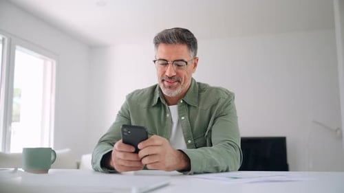 Man Using Smartphone at Desk in Bright Home