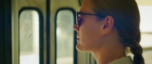 Woman wearing sunglasses standing inside a tram with sunlight streaming in