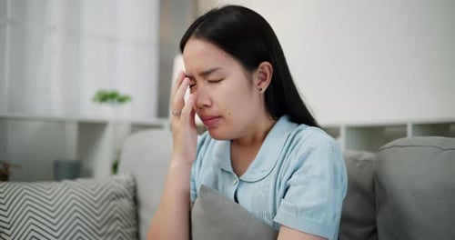 An unhappy young woman sits on a sofa, feeling stressed and thinking about something.