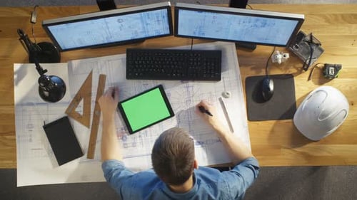 Top View of Architectural Engineer Draws on His Blueprints, Compares with Tablet Computer with Gree