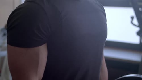 Broad-chested man performs bicep curls in gym with barbell, close-up