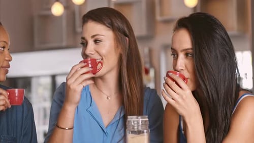 Three women laughing and drinking from mugs indoors