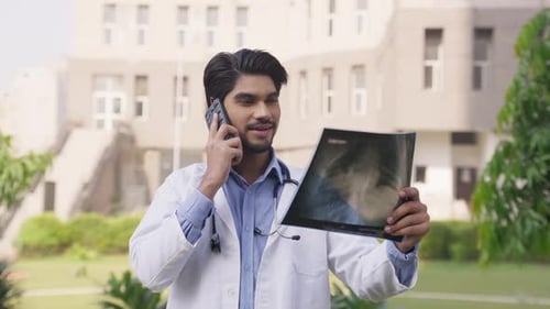 Médico indio feliz mirando un informe de rayos X y hablando por teléfono