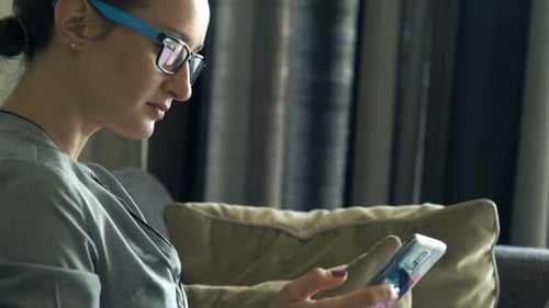 Woman Uses Laptop and Phone on Couch Indoors