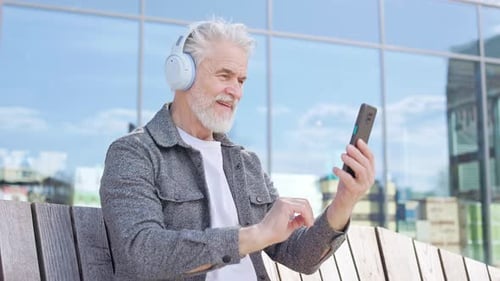 Glad Senior Man Scrolling and Typing on Smartphone in City