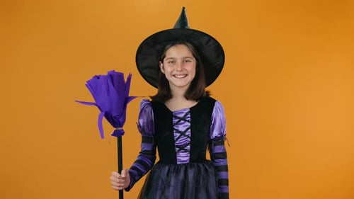 Smiling Child in Witch Costume Holding Broom