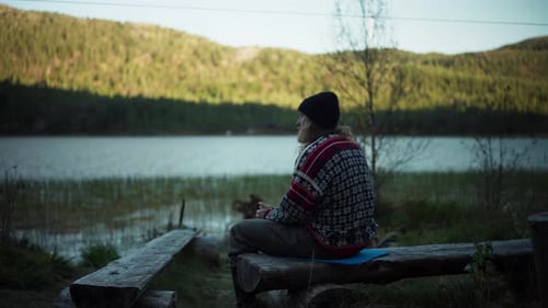 Man Sitting On Tree Trunk Bench While Drinking Coffee By The Lake In The Morning. - static shot