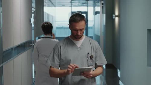 Hospital Worker Walking through Corridor and Using Digital Tablet