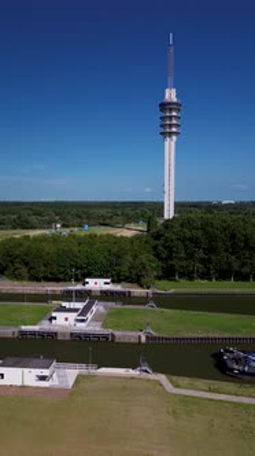 A tall communication tower rises above green landscapes and winding roads, captured in stunning