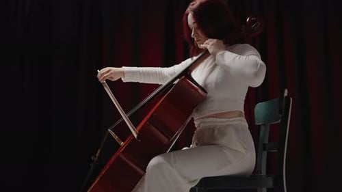 Woman Playing Cello in Dark Room with Red Curtains