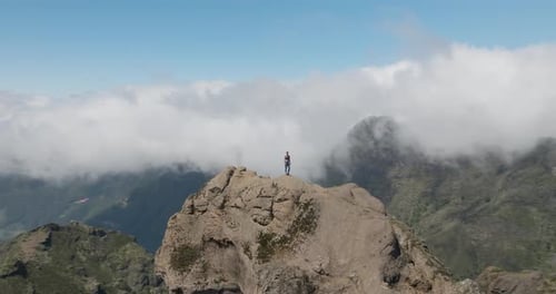 Woman on epic rock viewpoint in grand mountain range, aerial
