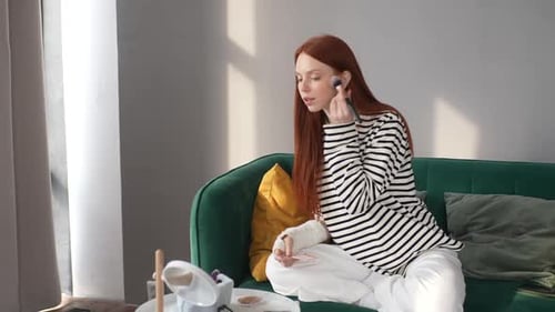 Woman Applies Makeup on Green Sofa at Home