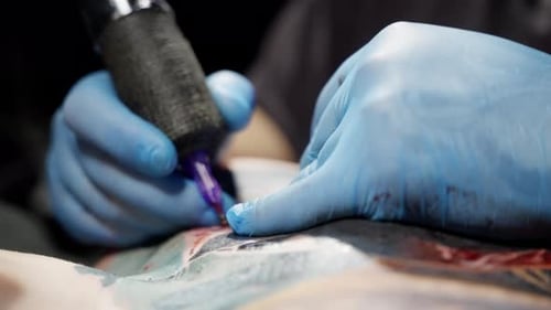 Tattoo Artist Wearing Blue Gloves Skillfully Operates a Tattoo Machine Creating Intricate Designs on